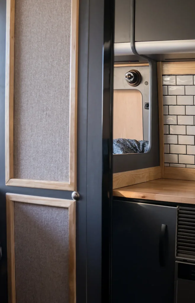 Interior de la furgoneta Fiat Ducato mostrando detalles de carpintería y tapicería en tonos claros y oscuros, destacando el contraste entre los paneles de madera y los acabados en negro.