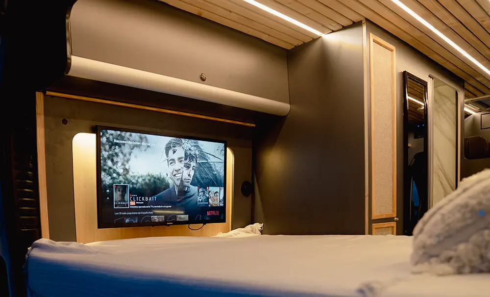 Vista interior del área de descanso en la Fiat Ducato, resaltando una cama espaciosa con cojines decorativos y una iluminación suave que crea una atmósfera acogedora.