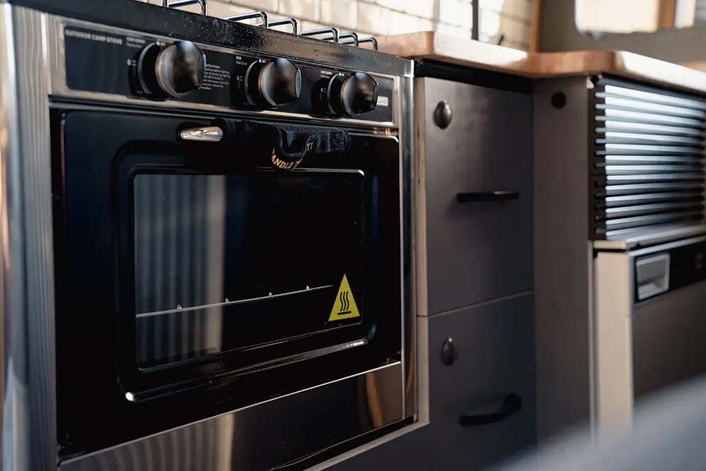 Área de cocina en la Fiat Ducato, mostrando un horno moderno con acabados en negro, situado debajo de una encimera de madera. A la derecha, un sistema de almacenamiento compacto aporta funcionalidad al espacio.