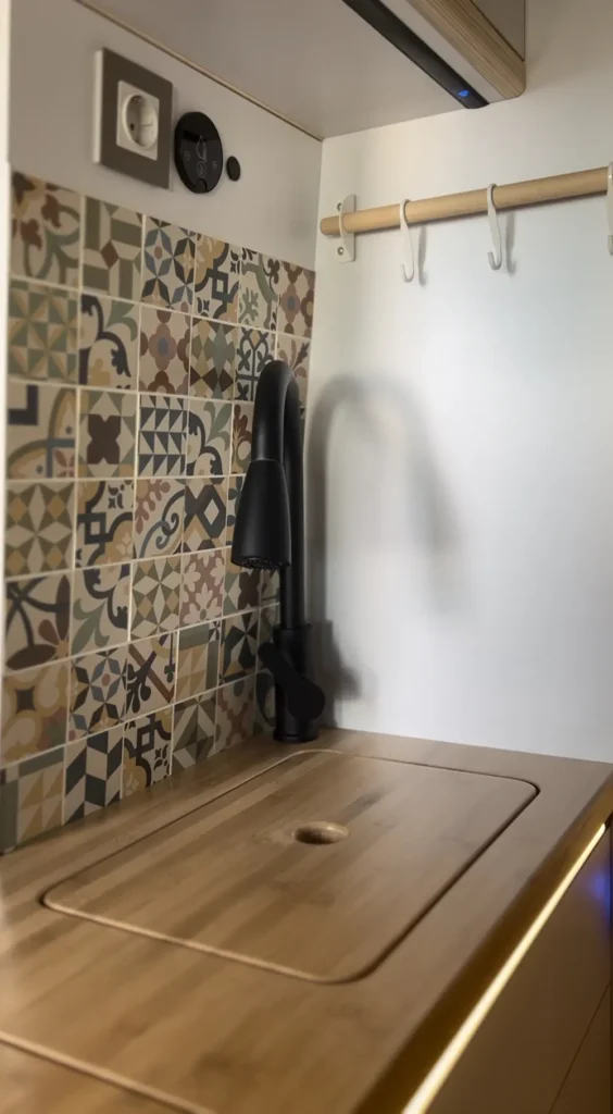 Cocina en una furgoneta Fiat Ducato con azulejos de colores vivos en estilo mediterráneo, mostrando un grifo moderno negro y encimeras de madera.